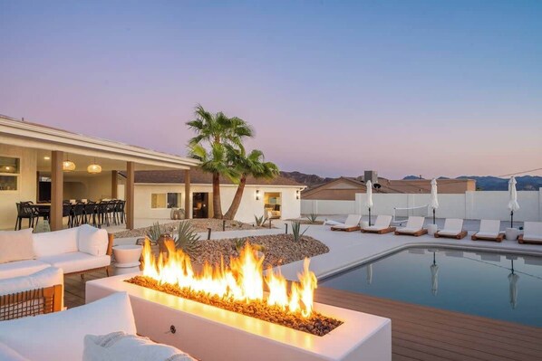 A pool area with lounge chairs, a fire feature, and a dining area with tables and chairs.