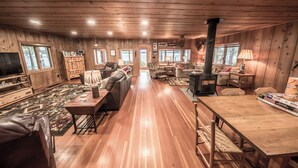 A cozy cabin interior with wooden walls, a fireplace, a TV, and a dining area.
