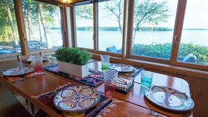 A dining table set with plates, glasses, and a plant, overlooking a lake.