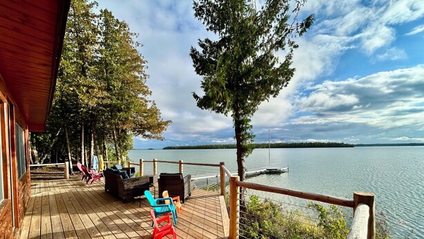 A wooden deck with outdoor furniture, a railing, and a view of a lake.