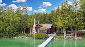 A cabin with a dock extending into a green lake, surrounded by trees.
