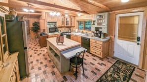 A wooden cabin interior with a kitchen, dining area, and a door with a window.