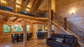 A spacious wooden cabin with a dining area, a living room with a leather sofa, and a staircase leading to a loft. - Scenic Ridge Lodge - Sleeps up to 16 - w/ Hot Tub (Logan)