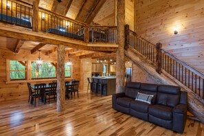Una cabaña de madera espaciosa con comedor, sala de estar con sofá de cuero y una escalera que sube a un altillo.