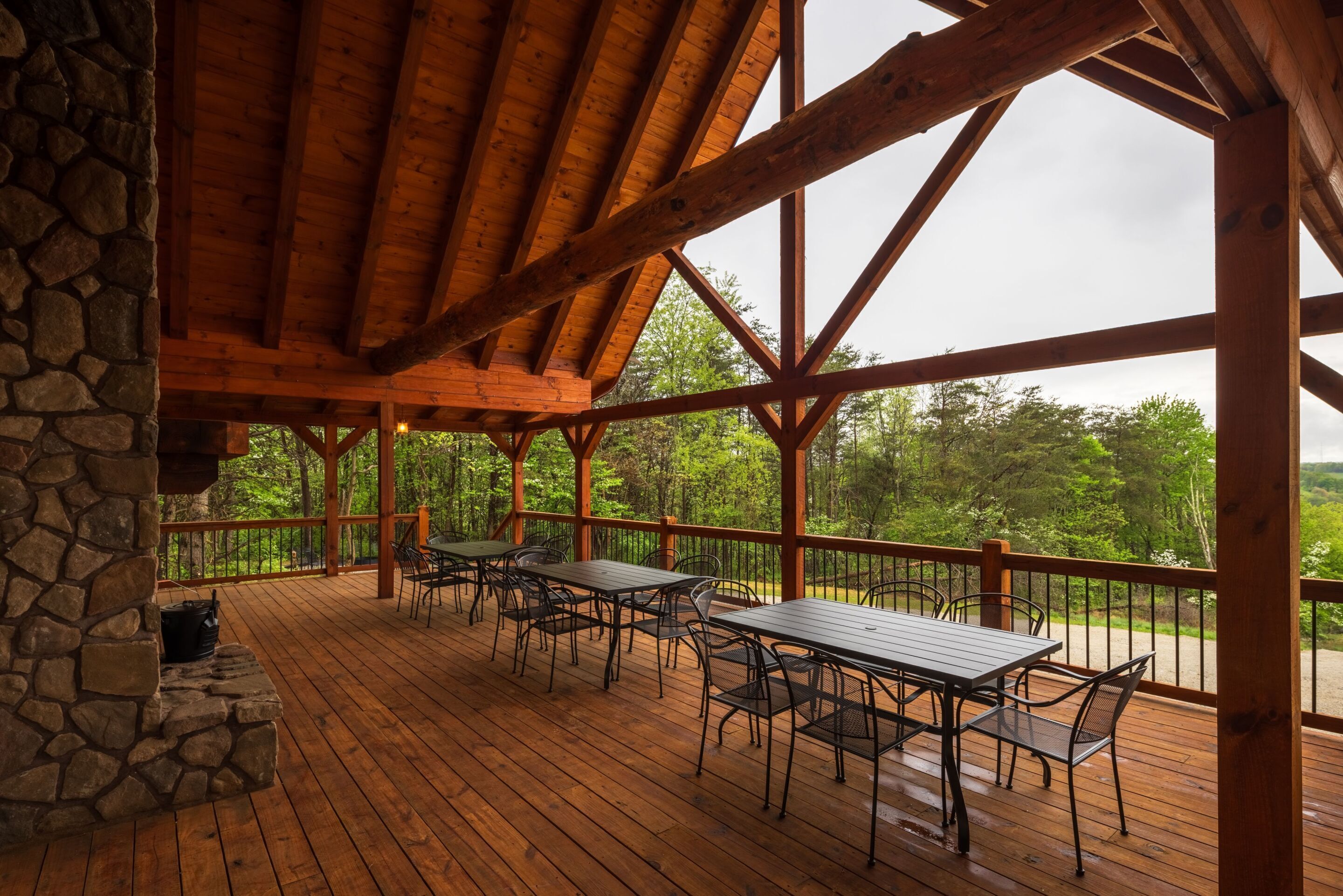 A covered outdoor deck with wooden flooring, stone walls, and metal tables and chairs.
