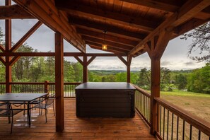 A wooden deck with a table and chairs, a hot tub, and a view of a forested landscape.