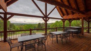 An outdoor wooden deck with tables and chairs, overlooking a green landscape.