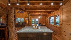 A wooden cabin interior with a kitchen island, dining area, and a large window overlooking the outdoors. - Scenic Ridge Lodge - Sleeps up to 16 - w/ Hot Tub (Logan)
