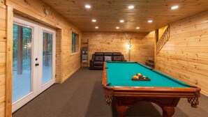 A wooden-paneled room with a pool table, a sofa, and a staircase.