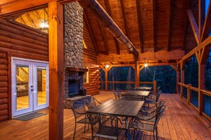 A log cabin with a stone fireplace, wooden deck, and outdoor seating area.