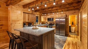 A wooden cabin interior with a kitchen featuring granite countertops, stainless steel appliances, and a bar area with stools. - Scenic Ridge Lodge - Sleeps up to 16 - w/ Hot Tub (Logan)