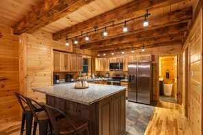 Interior de una cabaña de madera con cocina que cuenta con encimeras de granito, electrodomésticos de acero inoxidable y una zona de bar con taburetes.