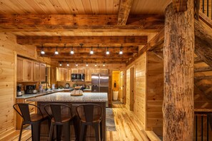 A wooden cabin interior with a kitchen featuring granite countertops, stainless steel appliances, and a central island with bar stools.