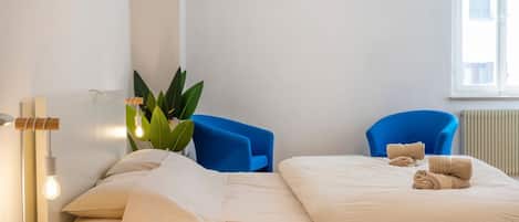 A hotel room with a bed, two blue chairs, a bedside table with a lamp, and a window with a view.