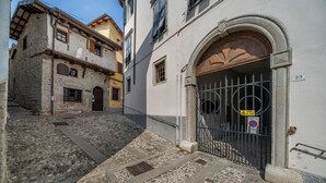 A narrow street with cobblestone pavement leading to a building with a large wooden door and a metal gate. - GuestHost - Cividale Medieval Town Apartment (Cividale del Friuli)