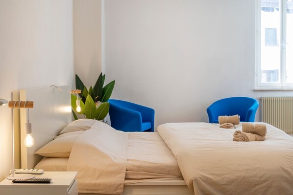 A hotel room with a bed, two blue chairs, a bedside table with a lamp, and a window with a view.