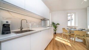 A modern kitchen with a built-in sink, a coffee machine, and a dining area with chairs and a table. - GuestHost - Cividale Medieval Town Apartment (Cividale del Friuli)