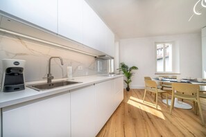 A modern kitchen with a built-in sink, a coffee machine, and a dining area with chairs and a table.