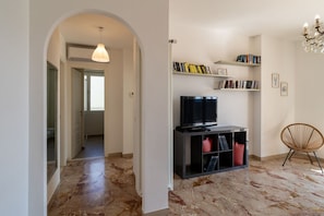 Een moderne woonkamer met een televisie, boekenplanken, een fauteuil en een marmeren vloer.
