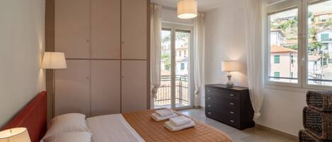 A hotel room with a bed, a dresser, a chair, and a view of the outside.