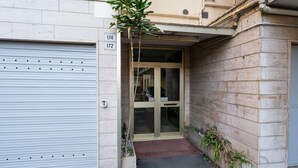 A building entrance with a closed garage door, a glass door entrance, and a small step leading to the door. - GuestHost - Splendid penthouse of 65 sqm located on the sixth floor of a residential building of the 70s with a wonderful terrace that offers views of the sea and the greenery. The apt. is located in via Lamarmora, a residential street above the famous t (Sanremo)