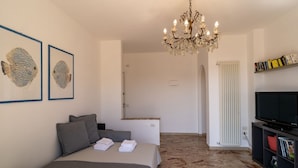 A bedroom with a bed, pillows, a chandelier, a television, and framed artwork on the wall. - GuestHost - Splendid penthouse of 65 sqm located on the sixth floor of a residential building of the 70s with a wonderful terrace that offers views of the sea and the greenery. The apt. is located in via Lamarmora, a residential street above the famous t (Sanremo)