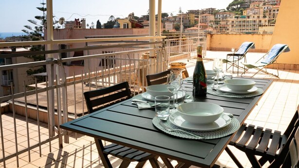 A rooftop terrace with a table set for two, a bottle of champagne, and two sun loungers. - GuestHost - Splendid penthouse of 65 sqm located on the sixth floor of a residential building of the 70s with a wonderful terrace that offers views of the sea and the greenery. The apt. is located in via Lamarmora, a residential street above the famous t (Sanremo)