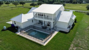 Una casa grande y blanca con piscina, mobiliario exterior y un patio amurallado.
