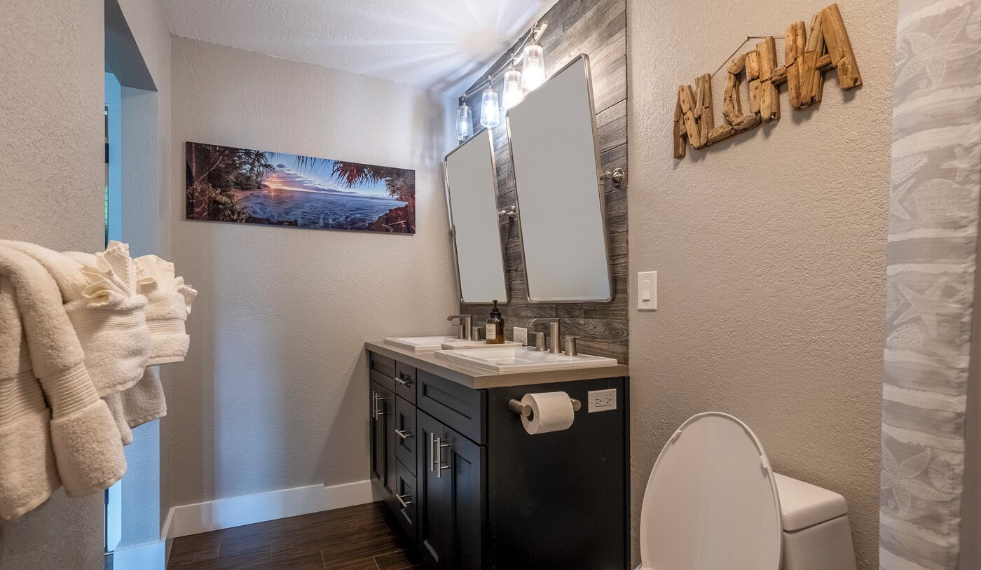 Un bagno con doppio lavabo, un water, un portasciugamani, uno specchio e un faretto a parete.