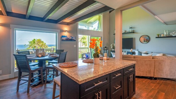 A modern kitchen with a large island, dark cabinetry, and a view of the outdoors. - Puamana 16B (Princeville)