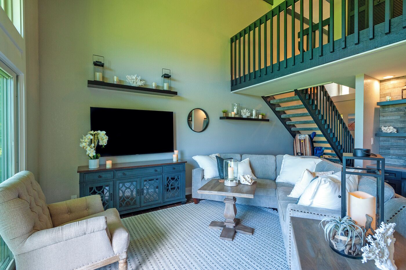 A living room with a large flat-screen TV, a sofa, a chair, a coffee table, and a staircase.