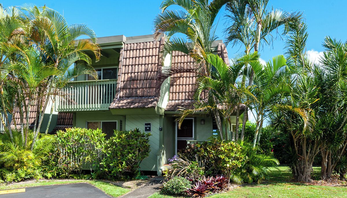 A two-story building with a balcony, surrounded by lush tropical vegetation.