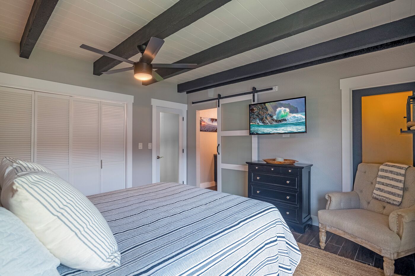 A bedroom with a bed, a chair, a TV, and a ceiling fan.
