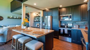 A modern kitchen with dark blue cabinets, stainless steel appliances, and a central island with stools. - Puamana 16B (Princeville)