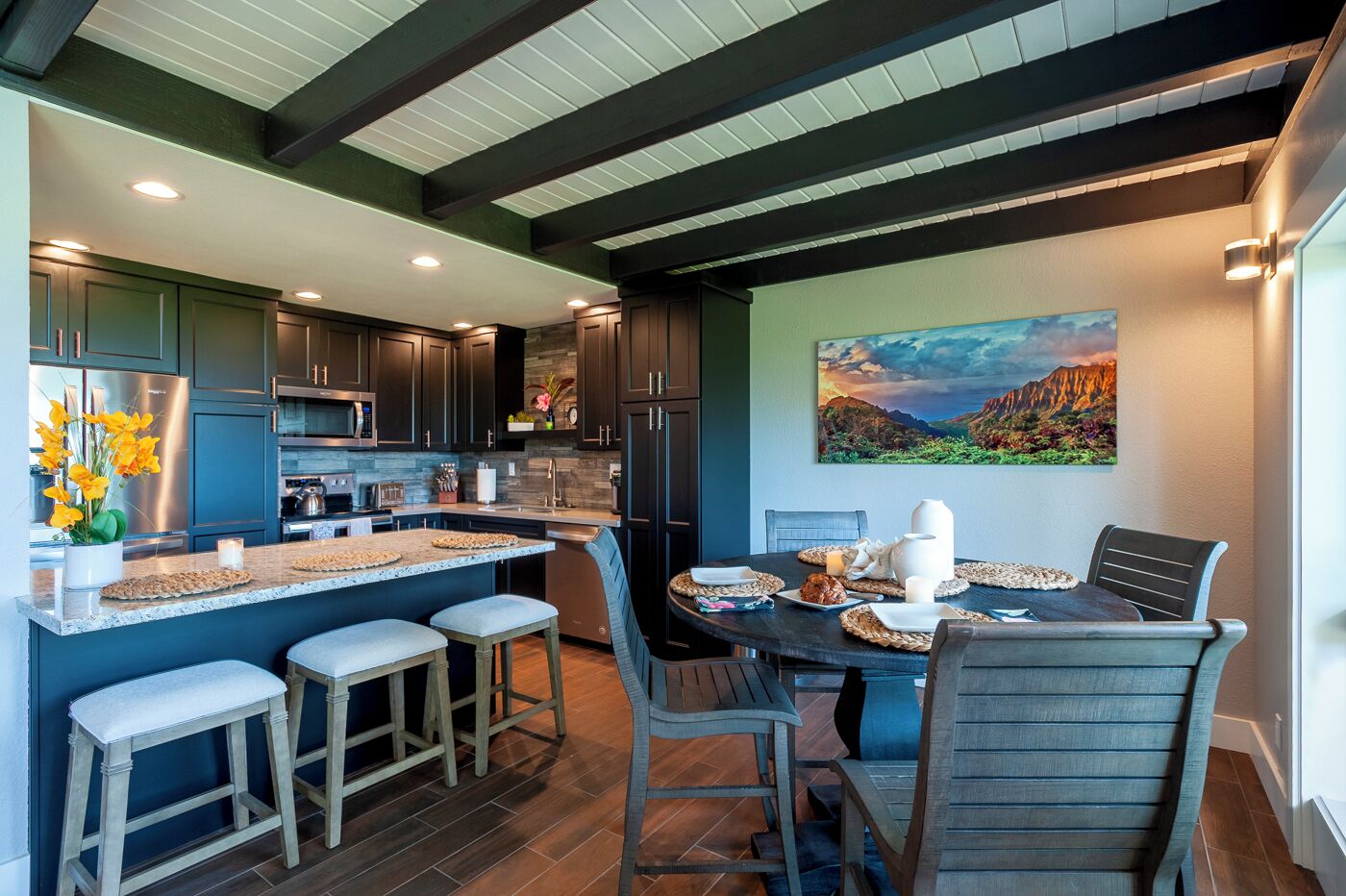 Una cocina moderna con armarios oscuros, una isla central con taburetes y una mesa de comedor preparada para cuatro personas.