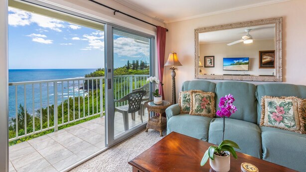 A balcony with a view of the ocean, a sofa with floral cushions, a lamp, and a mirror on the wall. - Alii Kai 4303 (Princeville)