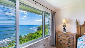 A hotel room with a large window offering a view of the ocean and greenery. - Alii Kai 4303 (Princeville)