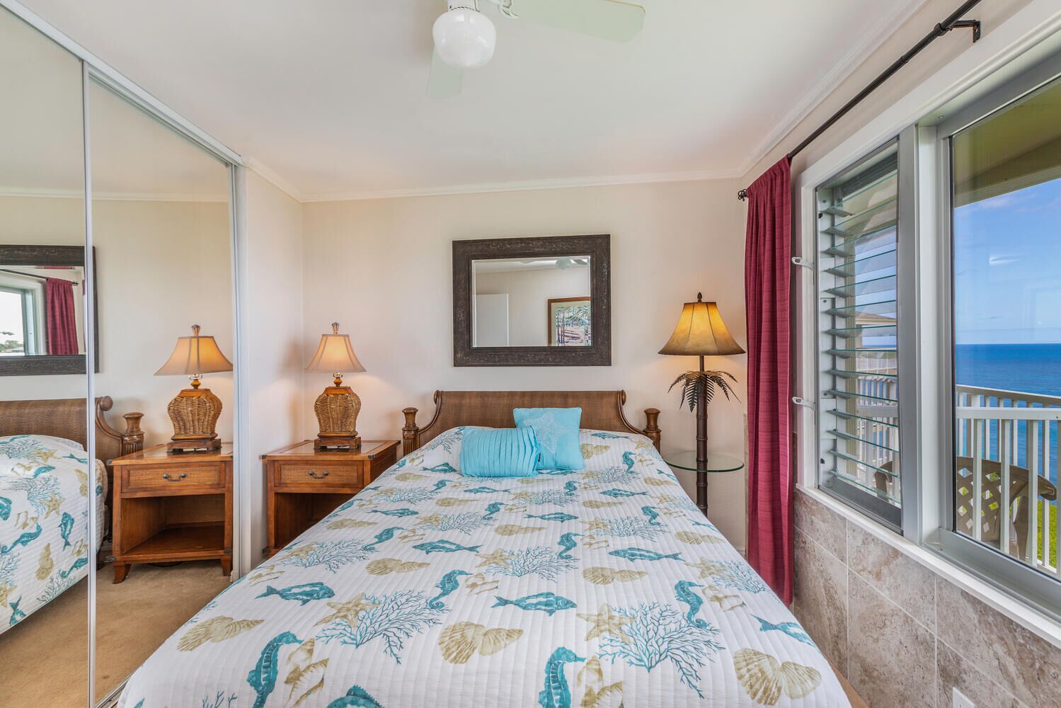 Quarto de hotel com cama, duas mesas de cabeceira, um criado-mudo, um espelho e uma janela com vista para o oceano.