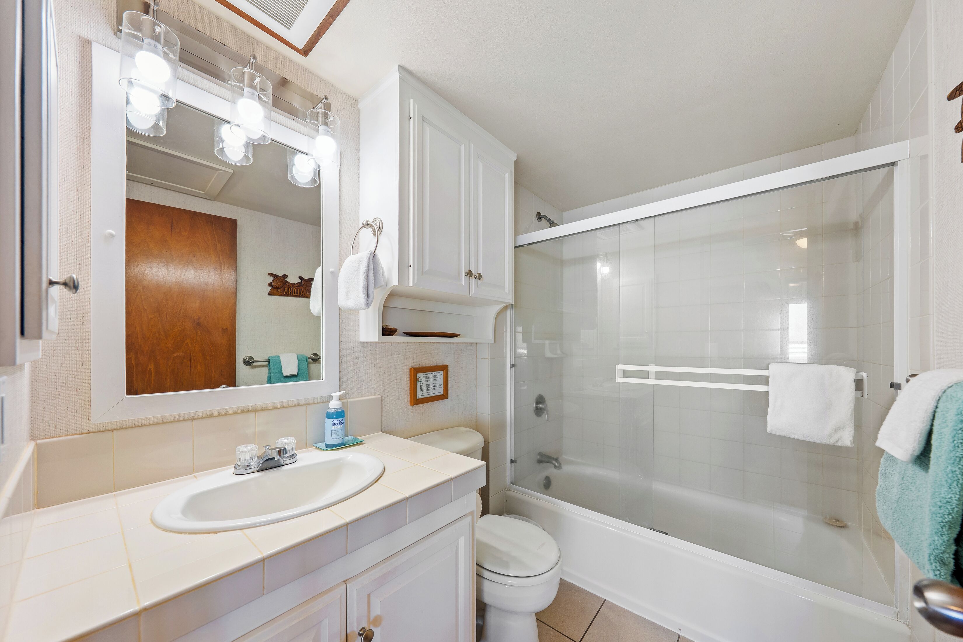 A bathroom with a sink, mirror, cabinet, toilet, and glass-enclosed shower.