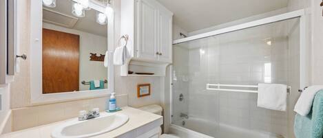 A bathroom with a sink, mirror, cabinet, toilet, and glass-enclosed shower.