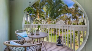 Eine Veranda mit Korbstühlen, einem kleinen Tisch und einer Buddha-Statue.
