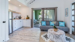 Eine moderne Küche mit weißen Schränken und einem Edelstahl-Kühlschrank, ein graues Sofa mit blauen Kissen und ein runder Couchtisch mit einem gewebten Mittelteil.