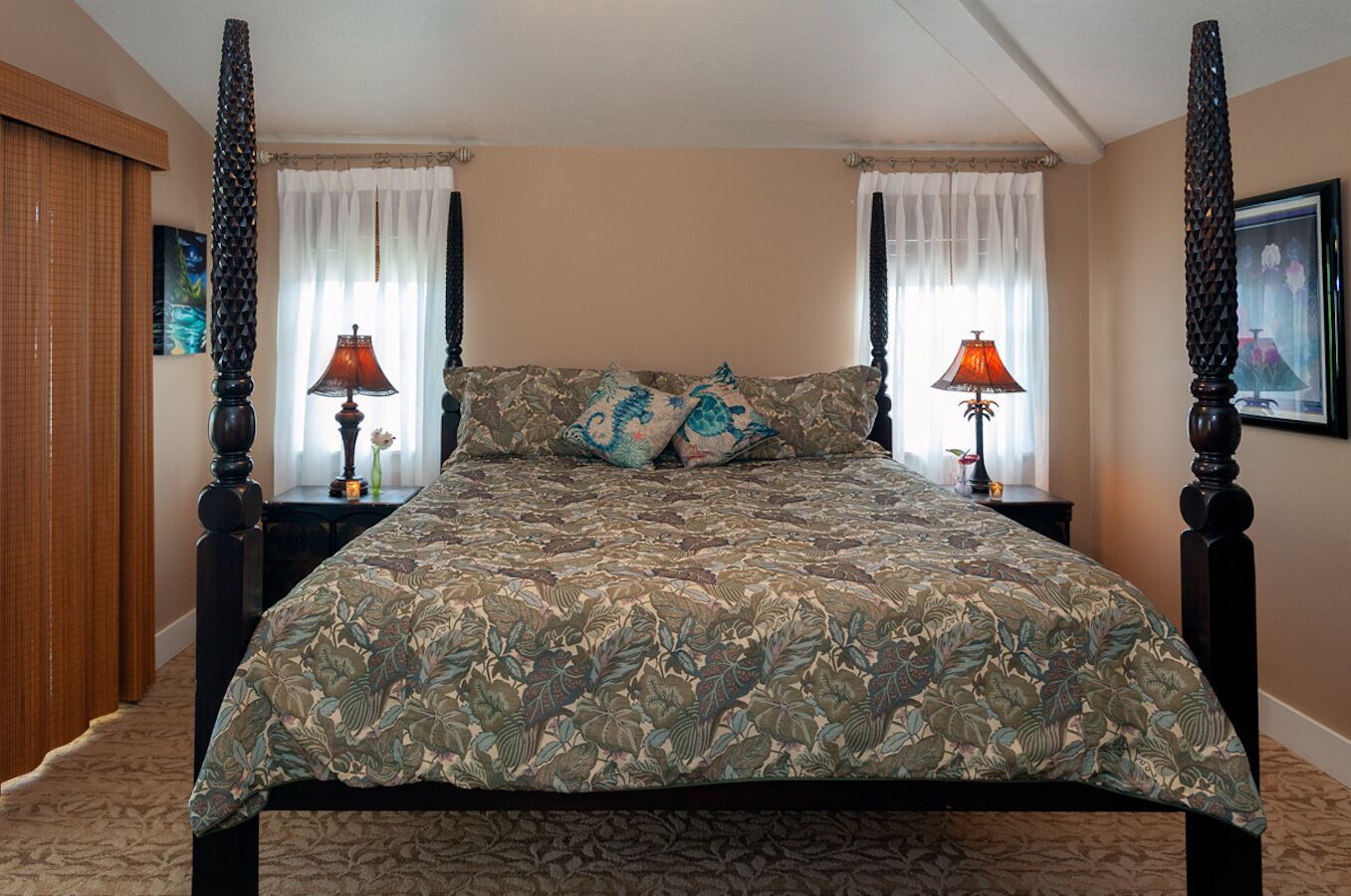 A four-poster bed with floral bedding, two bedside lamps, and a framed picture on the wall.