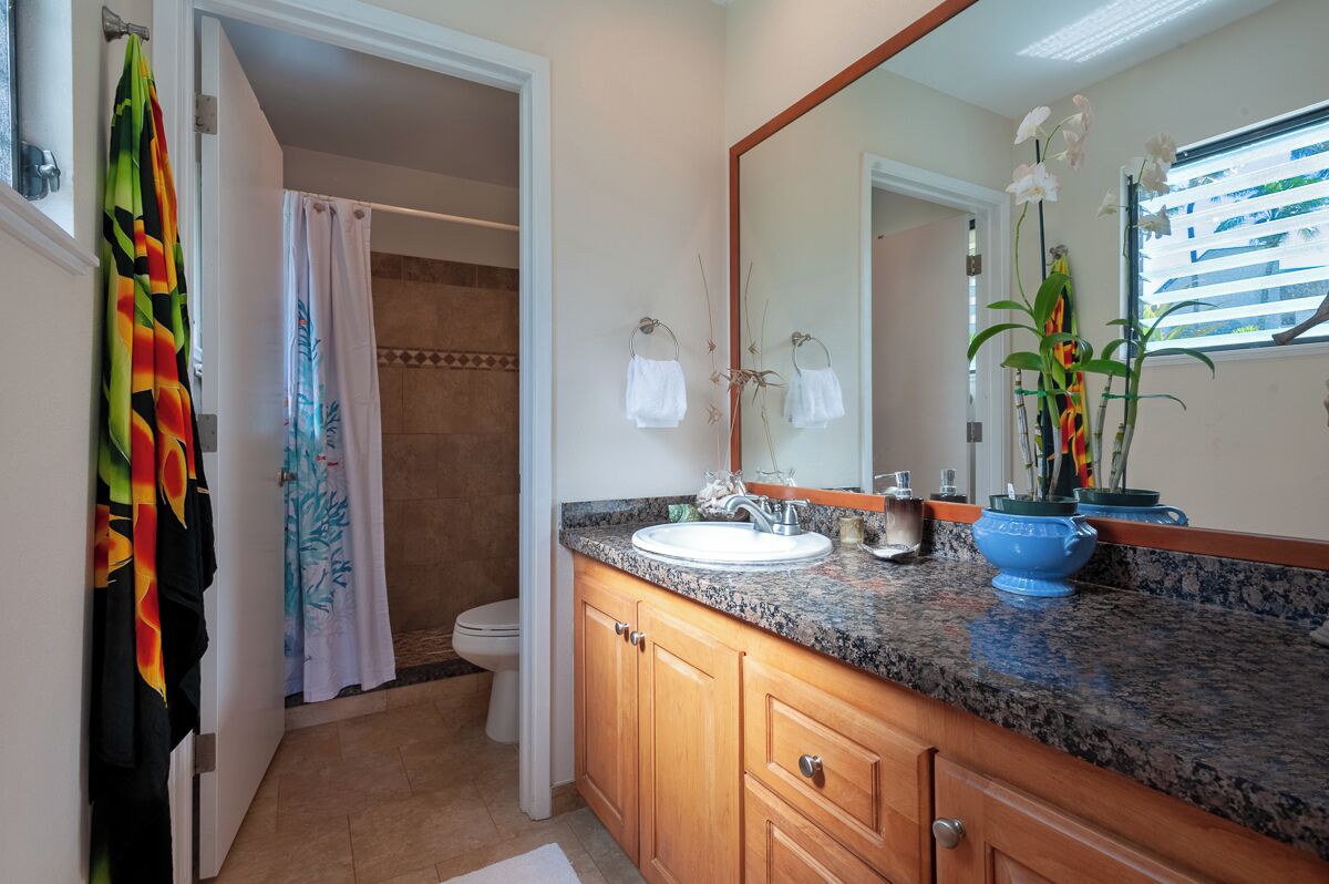 A bathroom with a granite countertop, wooden cabinets, a white sink, and a large mirror.