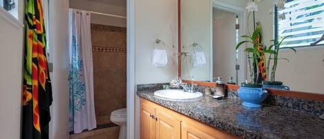 A bathroom with a granite countertop, wooden cabinets, a white sink, and a large mirror.