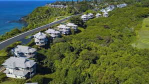 A coastal residential area with houses along a road, surrounded by lush greenery and the ocean. - Hanalei Bay Villa 26 (Princeville)