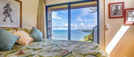 A bedroom with a large bed, a view of the sea, and framed pictures on the wall.