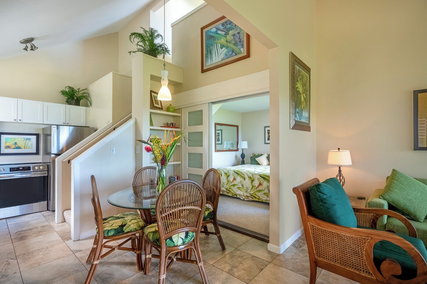A spacious kitchen with modern appliances, a dining area with wicker chairs, and a cozy living room with a green sofa.