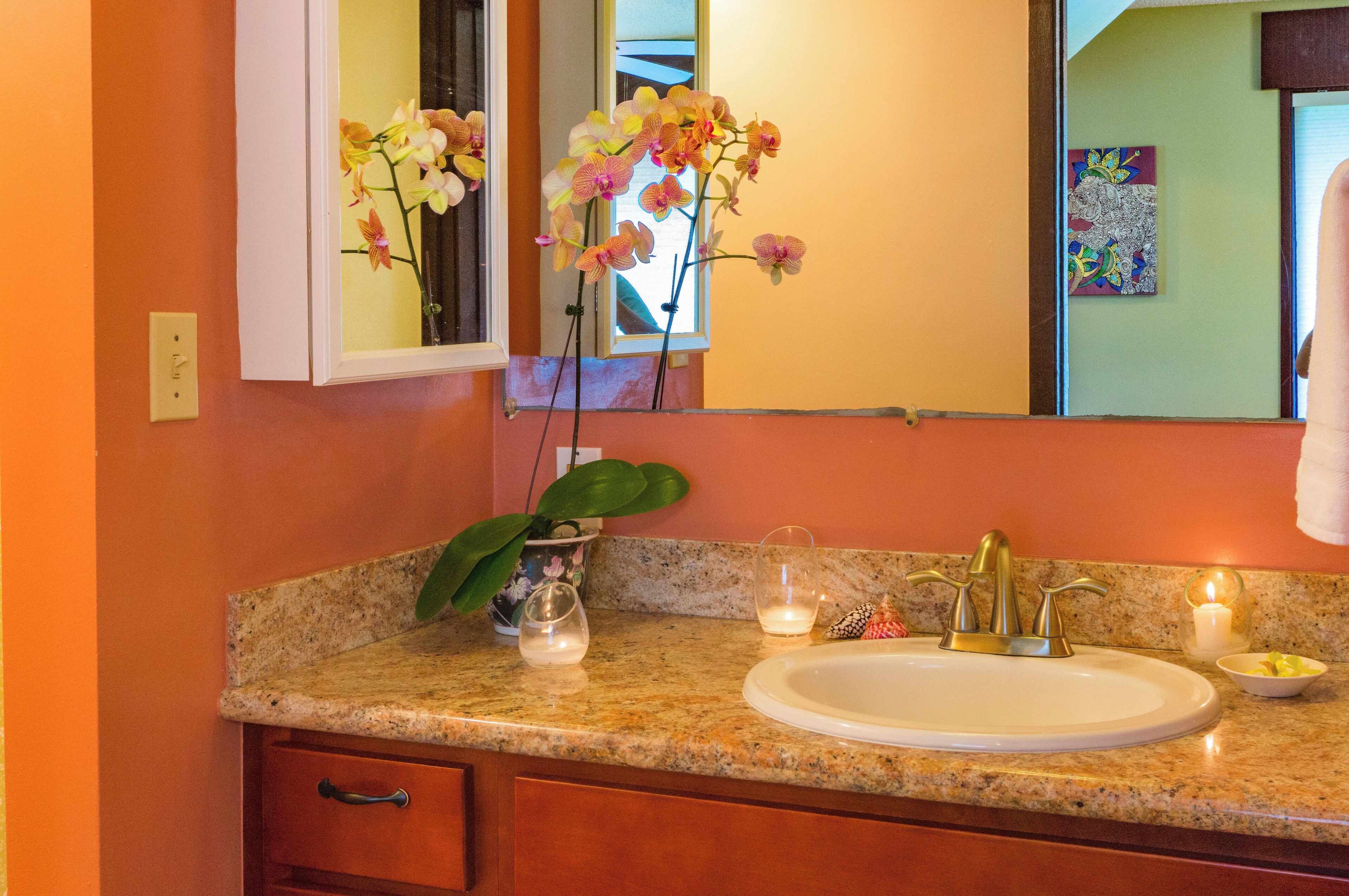 A bathroom with a granite countertop, a white sink, a mirror, and a potted plant.