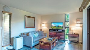 A living room with a sofa, coffee table, TV, and a small desk with a lamp. - Sealodge B4 (Princeville)